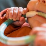 parent smiling and holding baby using a teething ring 